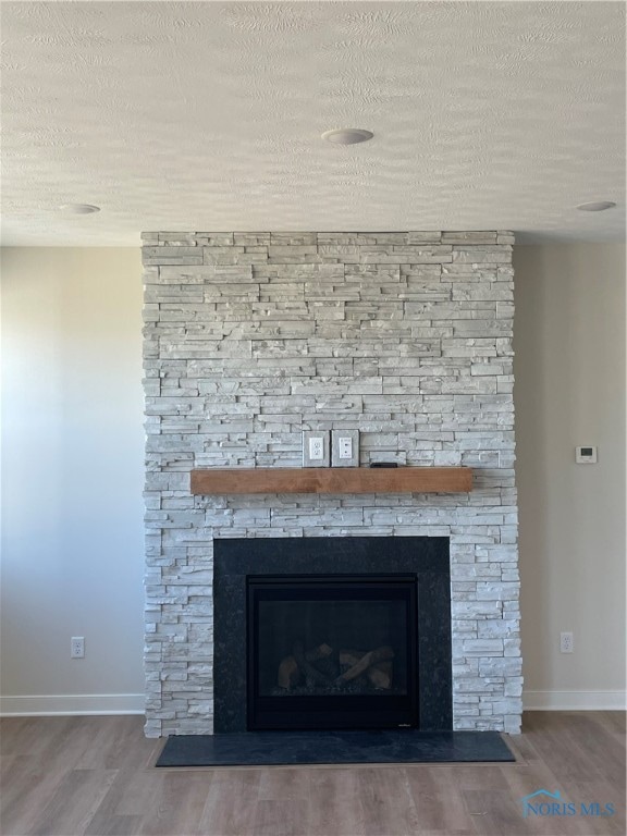 details with a textured ceiling, hardwood / wood-style flooring, and a stone fireplace