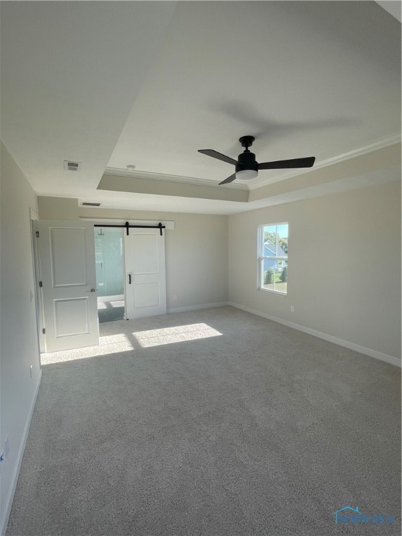 carpeted empty room featuring a barn door, a tray ceiling, and ceiling fan