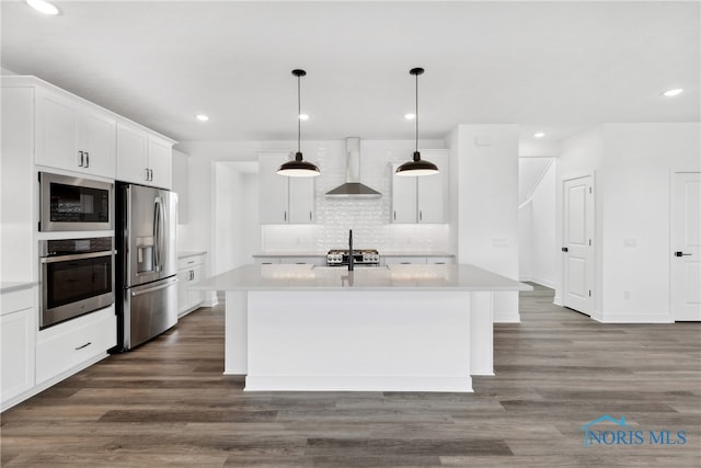 kitchen featuring white cabinetry, appliances with stainless steel finishes, decorative light fixtures, an island with sink, and wall chimney exhaust hood