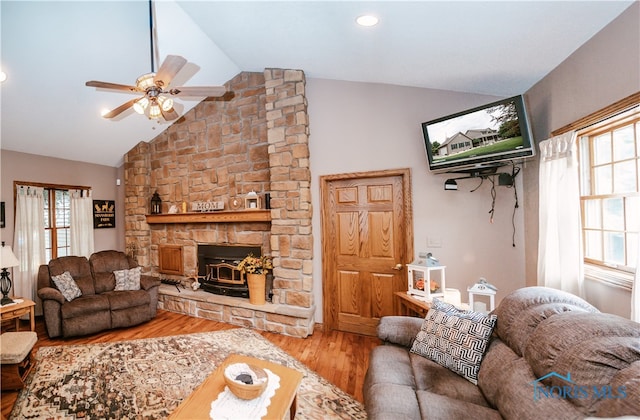 living room with hardwood / wood-style floors, a stone fireplace, vaulted ceiling, and ceiling fan