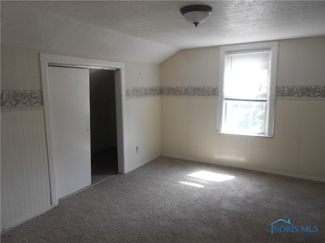 unfurnished bedroom featuring carpet flooring, lofted ceiling, a closet, and a textured ceiling