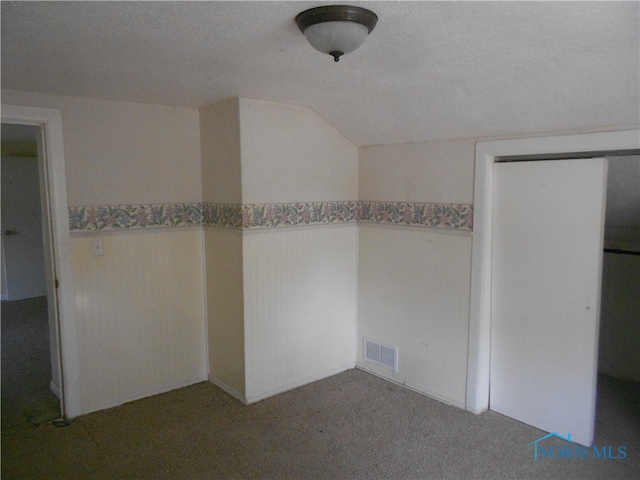 unfurnished bedroom with a textured ceiling, lofted ceiling, a closet, and dark carpet