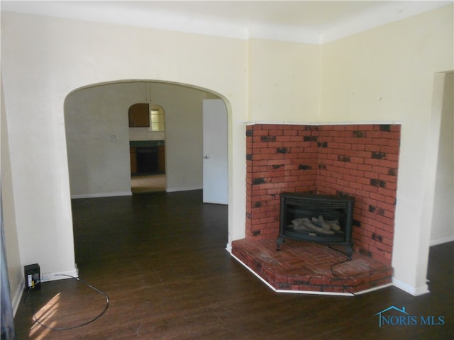 unfurnished living room with a brick fireplace, a wood stove, and dark hardwood / wood-style floors