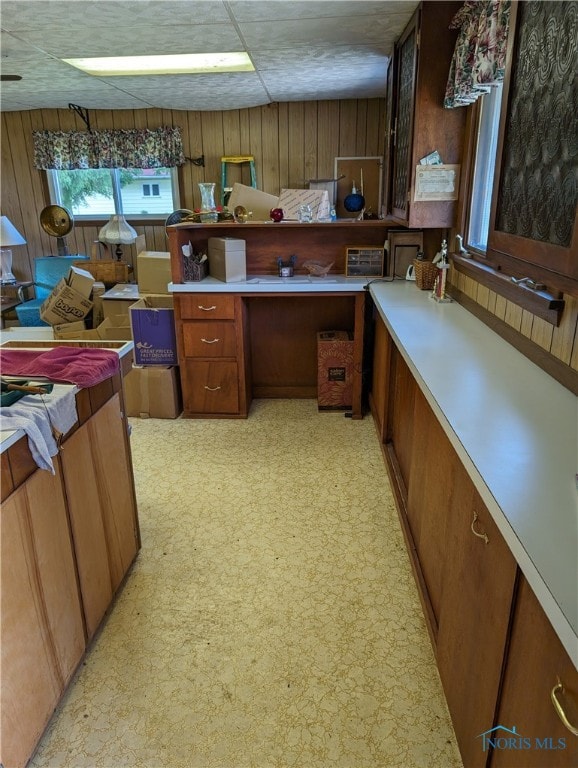 kitchen with built in desk, wood walls, light carpet, and a paneled ceiling