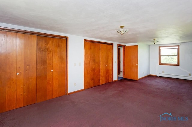 unfurnished bedroom with dark carpet, baseboard heating, and two closets