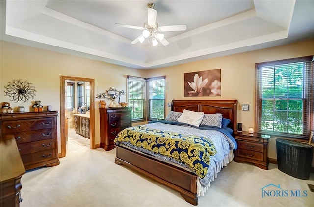 bedroom featuring light carpet, ceiling fan, a raised ceiling, and ensuite bath