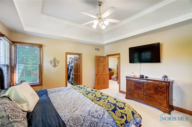 carpeted bedroom with a spacious closet, ceiling fan, a closet, and a tray ceiling