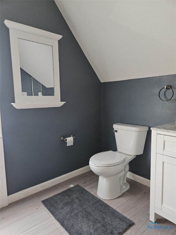 bathroom with vaulted ceiling, wood-type flooring, toilet, and vanity