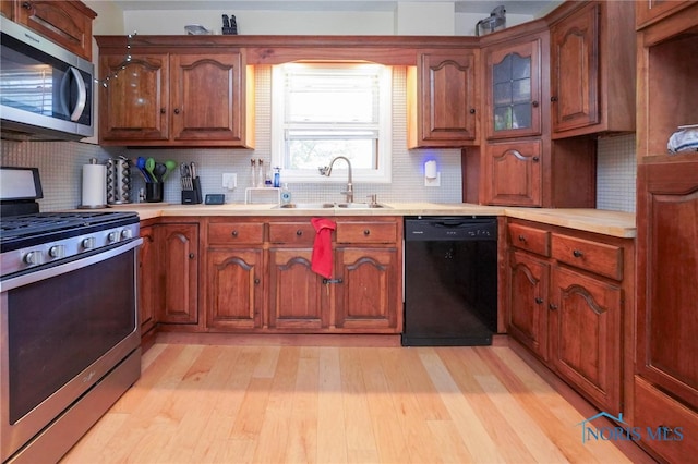 kitchen with stainless steel appliances, sink, tasteful backsplash, and light wood-type flooring