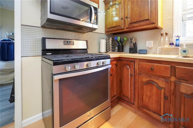 kitchen with appliances with stainless steel finishes, backsplash, and light wood-type flooring