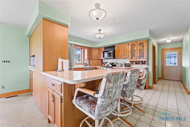 kitchen featuring kitchen peninsula, a breakfast bar, stainless steel stove, and light tile patterned floors