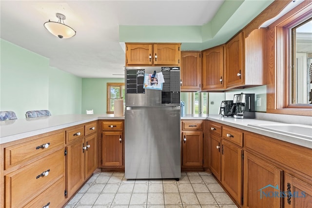 kitchen with a wealth of natural light, light tile patterned floors, kitchen peninsula, and stainless steel refrigerator