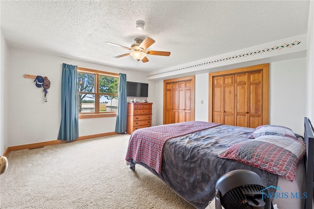 carpeted bedroom featuring a textured ceiling, ceiling fan, and multiple closets