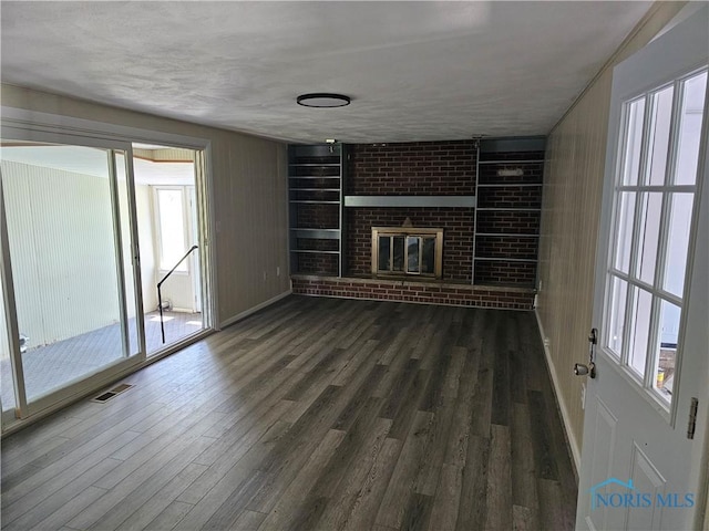 unfurnished living room with a textured ceiling, built in features, a fireplace, and dark wood-type flooring