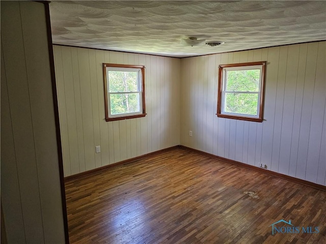 empty room with wooden walls, plenty of natural light, and dark wood-type flooring