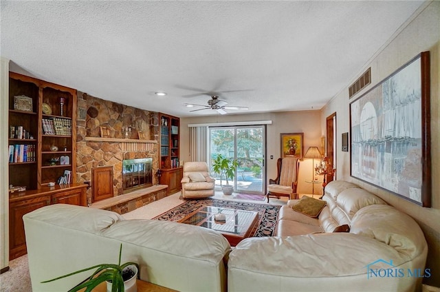 living room with ornamental molding, built in shelves, a textured ceiling, ceiling fan, and a fireplace