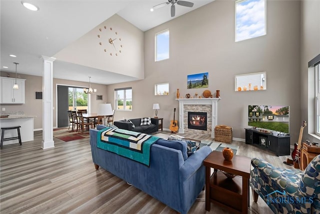 living room with hardwood / wood-style flooring, a fireplace, ceiling fan with notable chandelier, and decorative columns