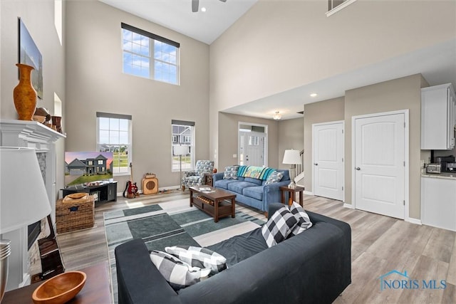 living room featuring ceiling fan, light hardwood / wood-style flooring, and a high ceiling