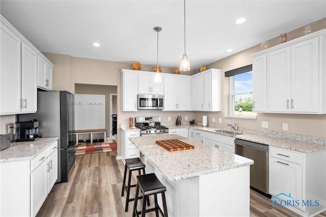 kitchen with stainless steel appliances, white cabinetry, a center island, and decorative light fixtures