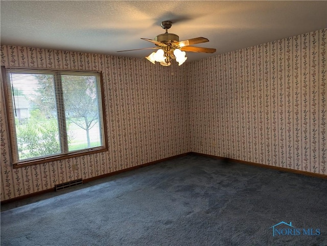 spare room featuring ceiling fan, dark carpet, and a textured ceiling