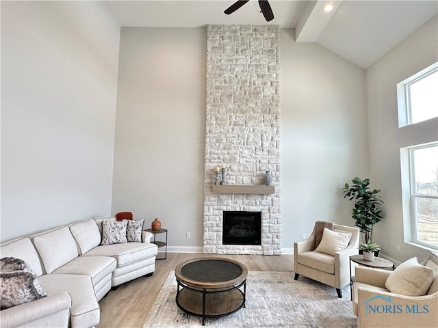 living room featuring vaulted ceiling, a healthy amount of sunlight, a stone fireplace, and light wood-type flooring