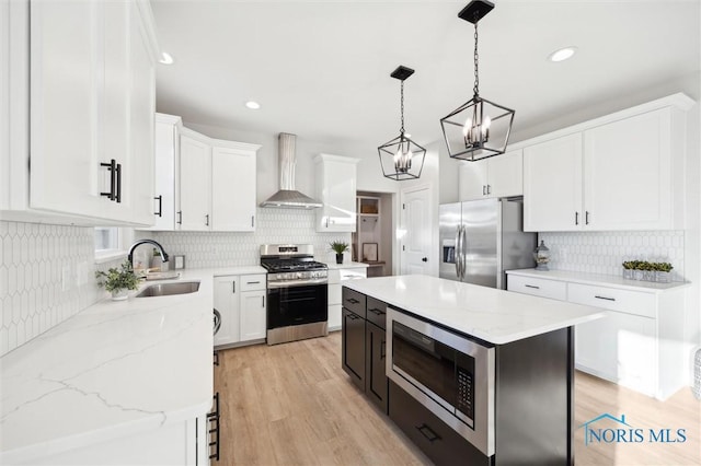 kitchen with light wood finished floors, a sink, white cabinets, appliances with stainless steel finishes, and wall chimney range hood