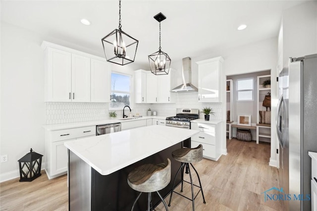 kitchen featuring a sink, light wood-style floors, appliances with stainless steel finishes, wall chimney exhaust hood, and tasteful backsplash