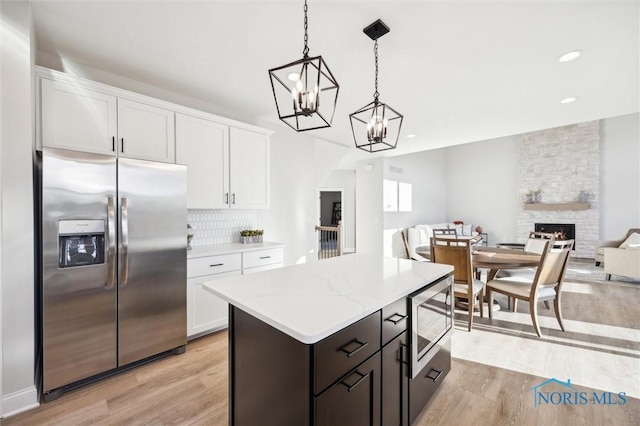 kitchen with a stone fireplace, white cabinets, light wood finished floors, and stainless steel appliances