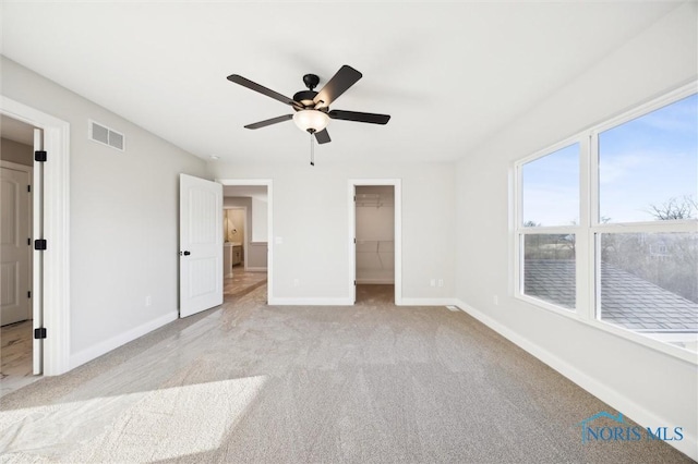 unfurnished bedroom featuring visible vents, a walk in closet, ceiling fan, baseboards, and carpet floors