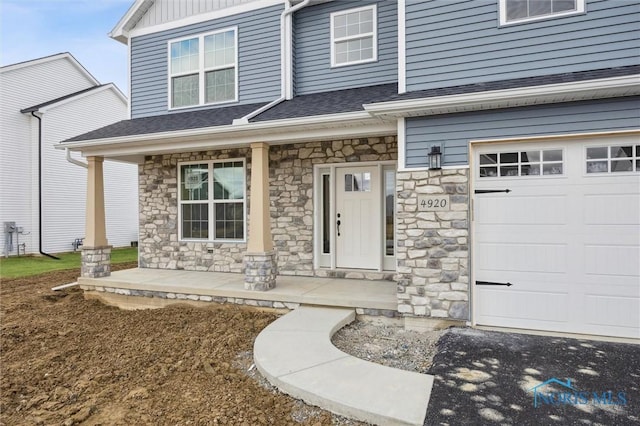 doorway to property featuring covered porch, a shingled roof, a garage, stone siding, and board and batten siding