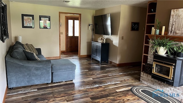 living room with a brick fireplace, a textured ceiling, and dark hardwood / wood-style flooring