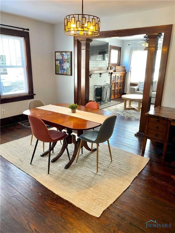 dining space featuring ceiling fan with notable chandelier, dark hardwood / wood-style flooring, and a brick fireplace