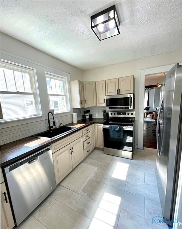 kitchen with tasteful backsplash, stainless steel appliances, sink, light tile patterned floors, and a textured ceiling