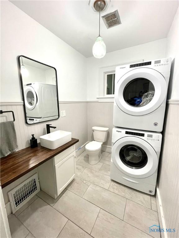 washroom with light tile patterned floors, stacked washer / dryer, and sink