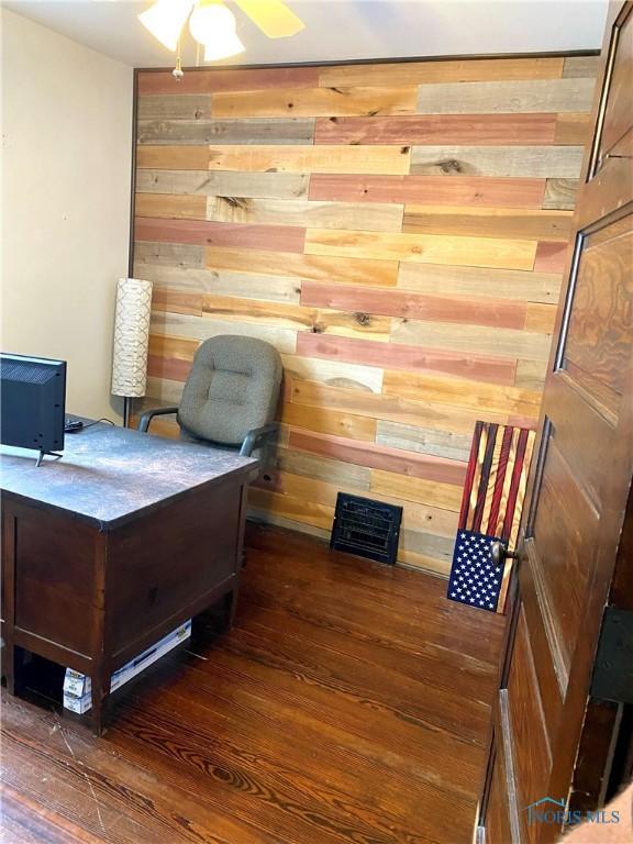 home office with wooden walls, ceiling fan, and dark hardwood / wood-style floors