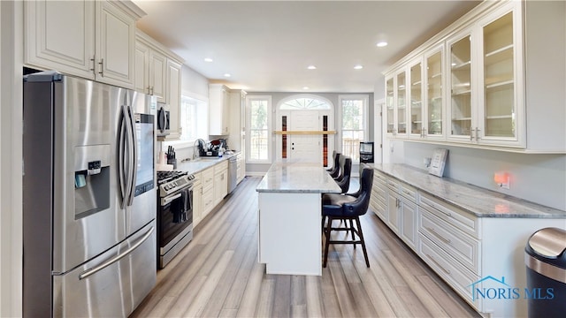 kitchen featuring white cabinetry, light wood-type flooring, light stone countertops, appliances with stainless steel finishes, and a kitchen bar