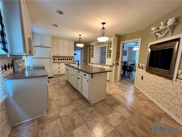 kitchen with sink, range, white cabinets, a center island with sink, and decorative light fixtures