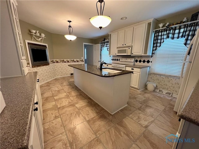 kitchen featuring pendant lighting, sink, white appliances, dark stone countertops, and an island with sink