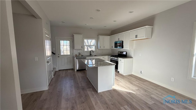 kitchen with sink, white cabinetry, a kitchen island, stainless steel appliances, and light stone countertops