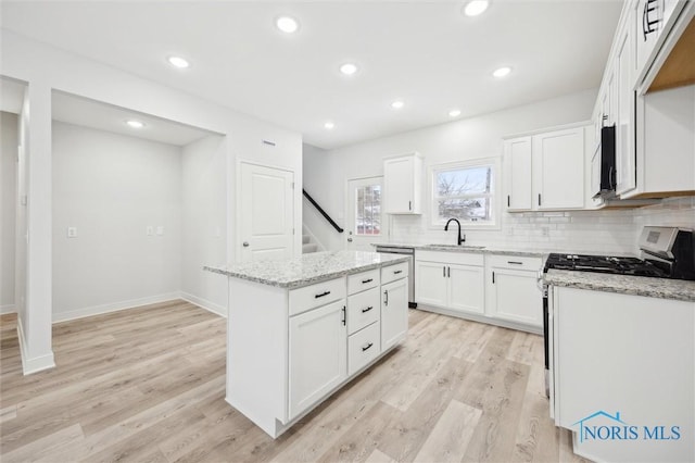 kitchen with sink, a center island, light wood-type flooring, light stone countertops, and white cabinets