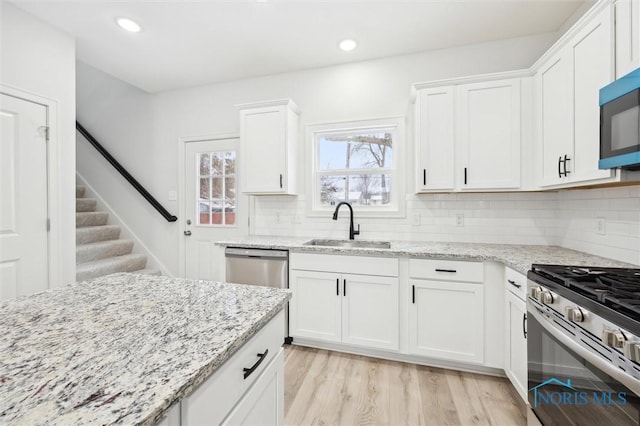 kitchen with sink, white cabinetry, stainless steel appliances, tasteful backsplash, and light stone countertops