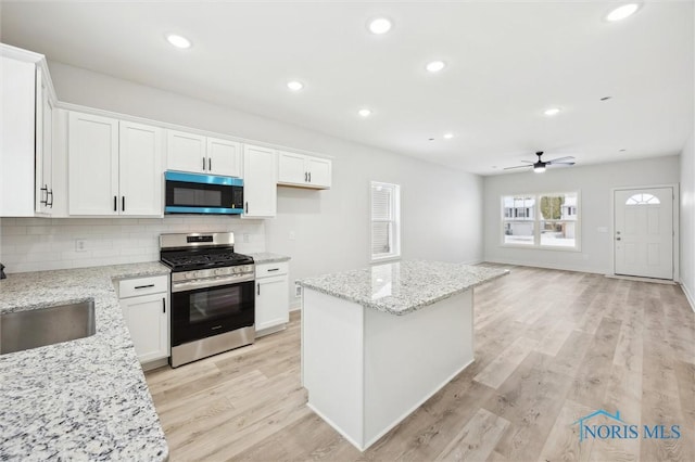 kitchen with sink, gas range, white cabinetry, a center island, and light stone countertops