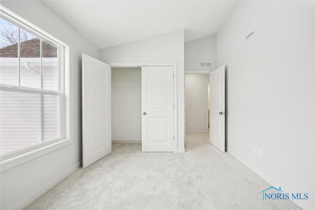 unfurnished bedroom featuring lofted ceiling, light carpet, and a closet