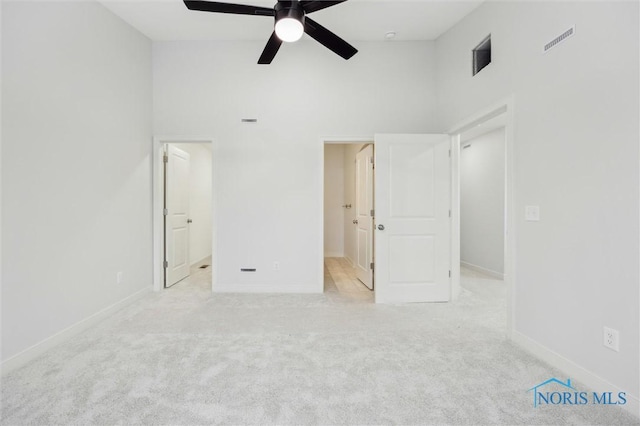 unfurnished bedroom featuring light carpet, ceiling fan, and a high ceiling