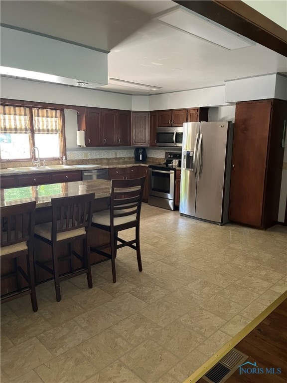 kitchen with appliances with stainless steel finishes, sink, backsplash, and a kitchen bar