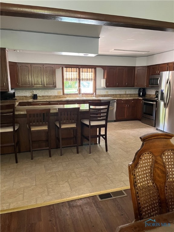 kitchen with backsplash, a breakfast bar area, light hardwood / wood-style floors, and appliances with stainless steel finishes