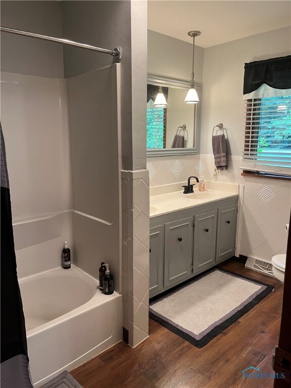 full bathroom with tile walls, hardwood / wood-style floors, vanity, and shower / bath combination with curtain