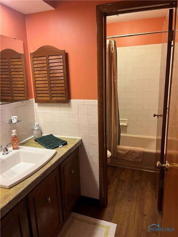 full bathroom with toilet, shower / tub combo, tile walls, vanity, and hardwood / wood-style flooring