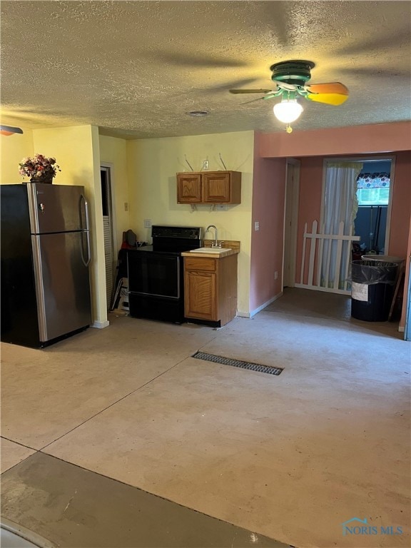 kitchen featuring black range with electric stovetop, sink, stainless steel refrigerator, and a textured ceiling