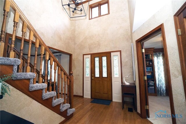 entrance foyer featuring a towering ceiling, wood-type flooring, a notable chandelier, and a wealth of natural light